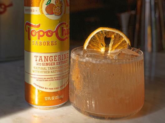 A can of Topo Chico Sabores Tangerine Hibiscus next to a glass with the Topo Toddy drink