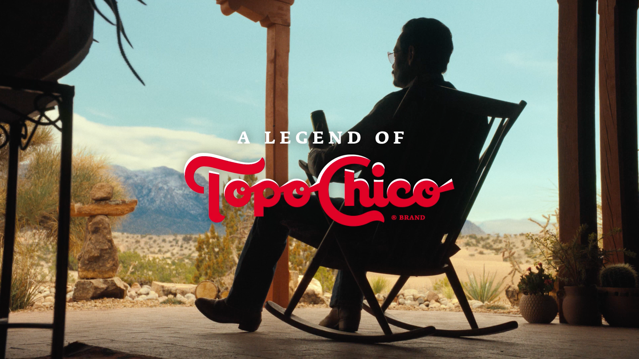 a silhouette of a man sitting in a rocking chair on a porch in the desert
