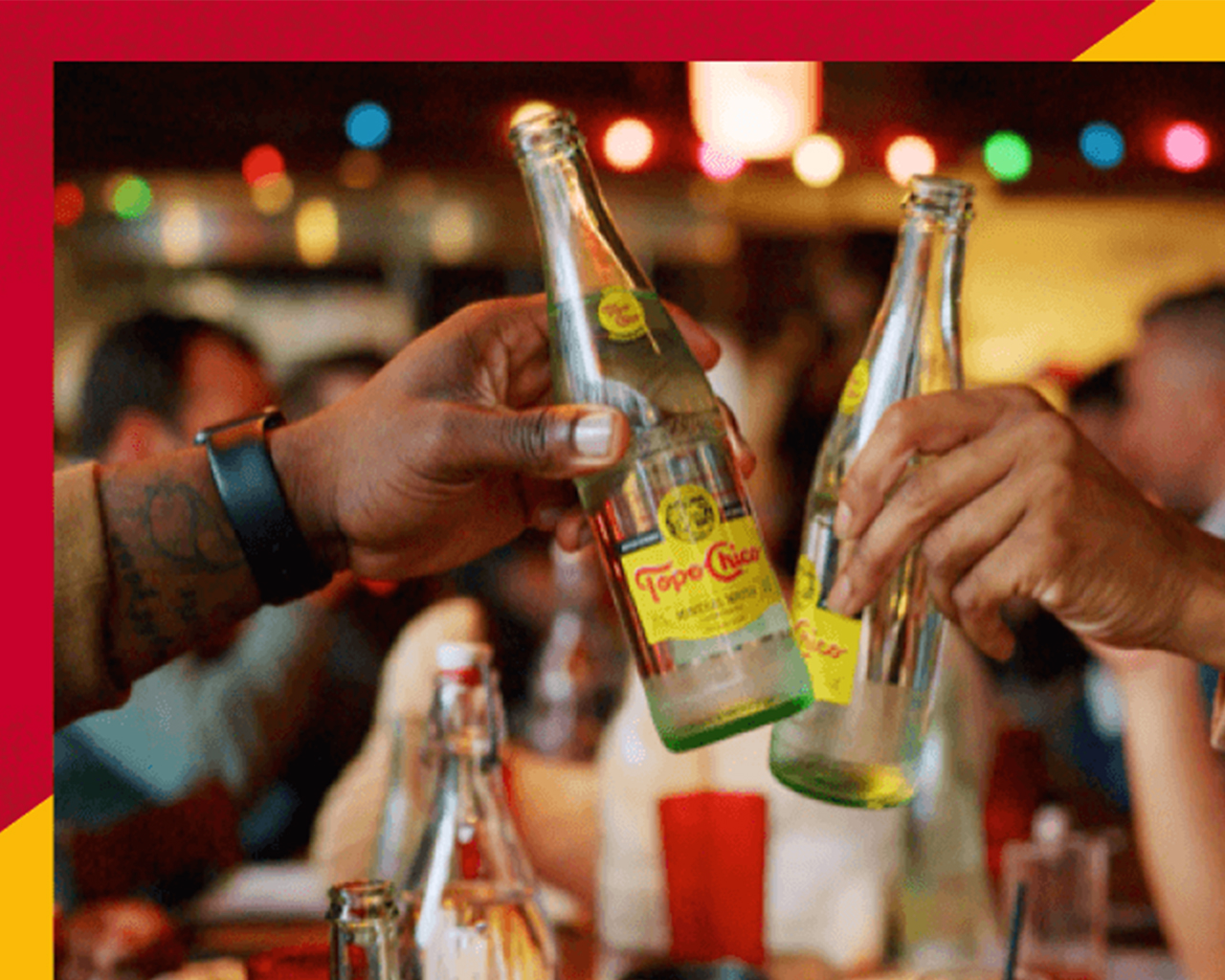 Close up of two hands toasting with two Topo Chico bottles