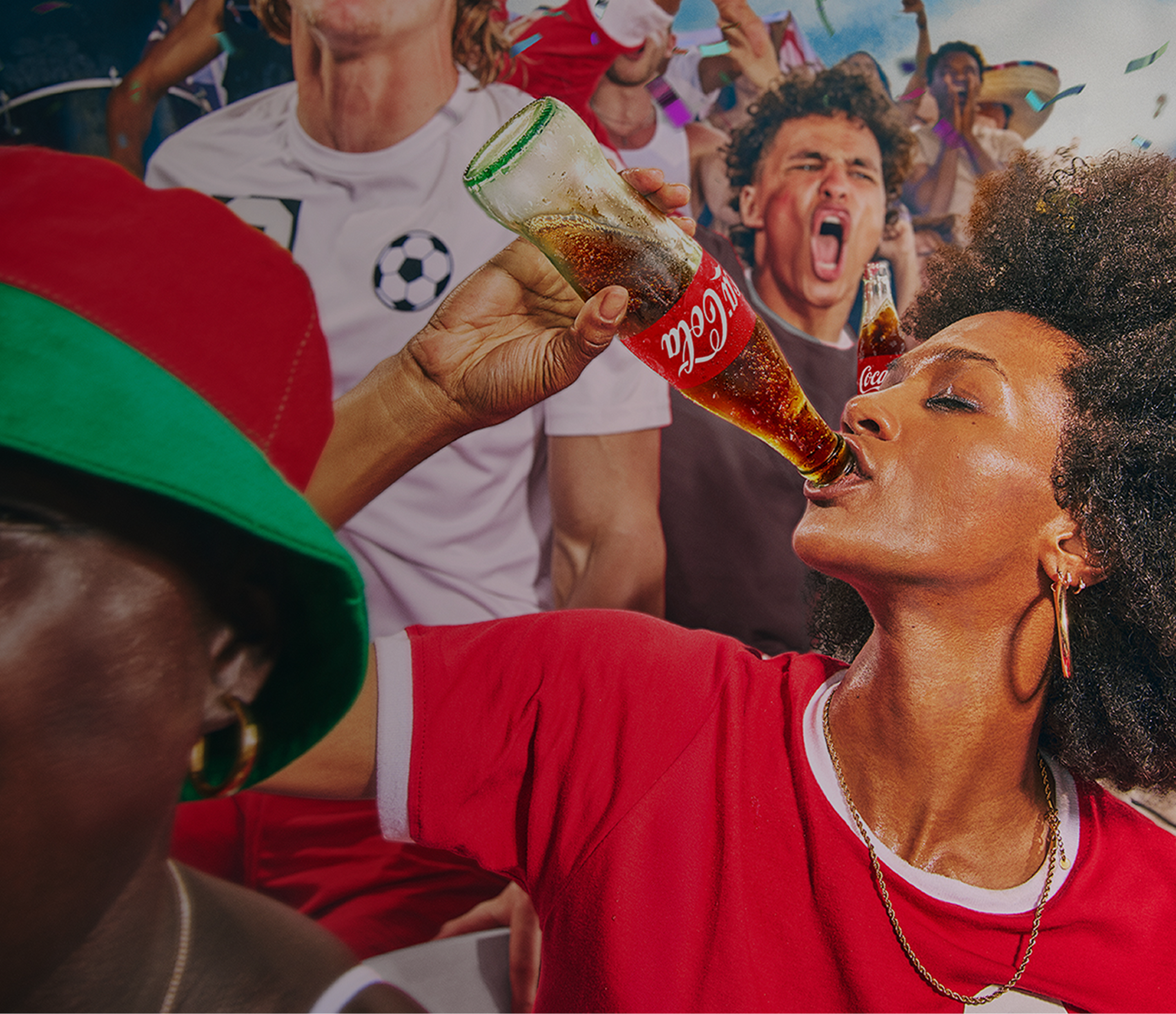 A female soccer fan in a red shirt drinks from a glass Coca-Cola bottle while surrounded by a cheering crowd.