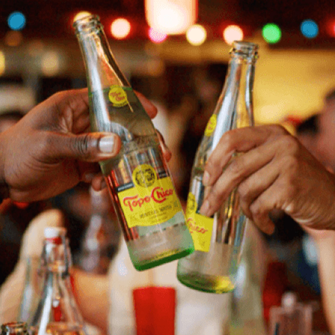 Close up of two hands toasting with two Topo Chico bottles