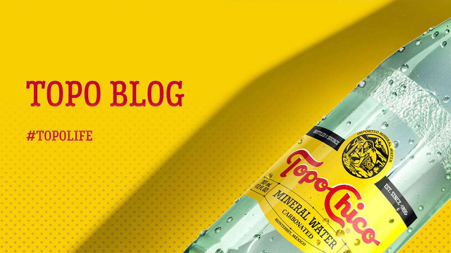 A Topo-Chico bottle on top of a yellow surface with 'Topo Blog' and '#TOPOLIFE'adisplayed in red letters on the side