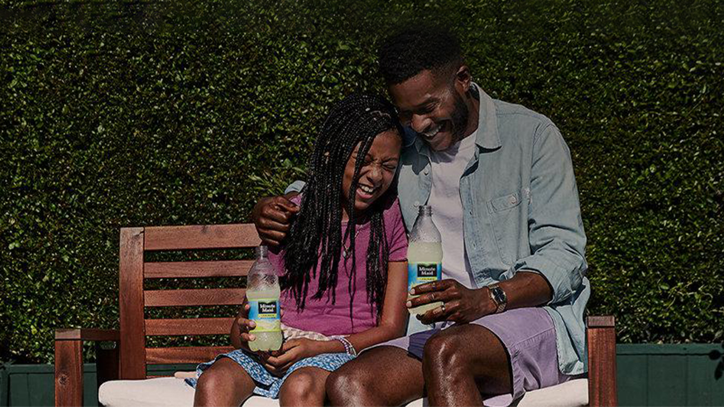 A father and daughter laughing together holding a bottle of Minute Maid