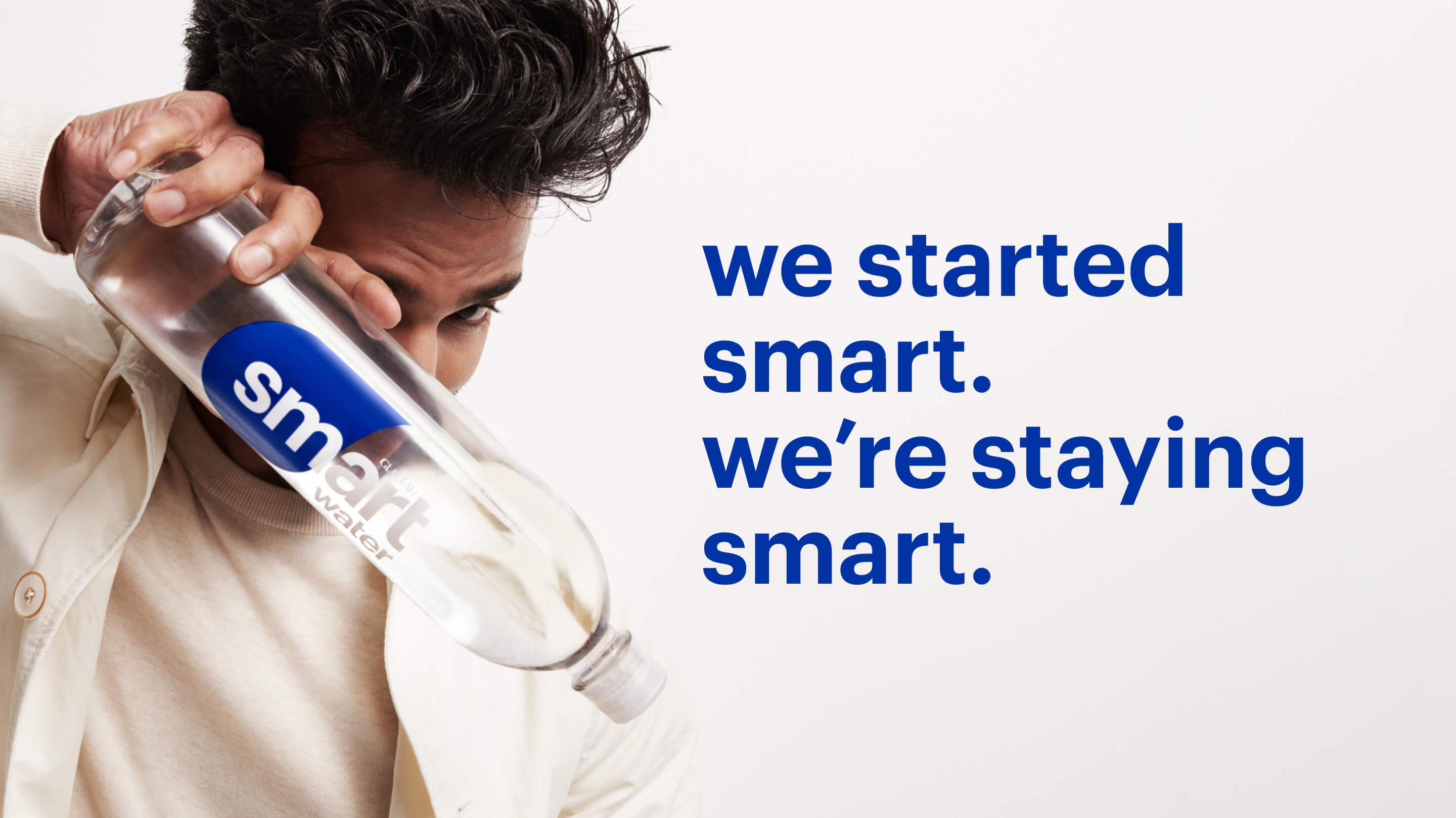 Man holding a Glacéau Smartwater bottle in front of his face right next to the phrase "we start smart. we're staying smart".