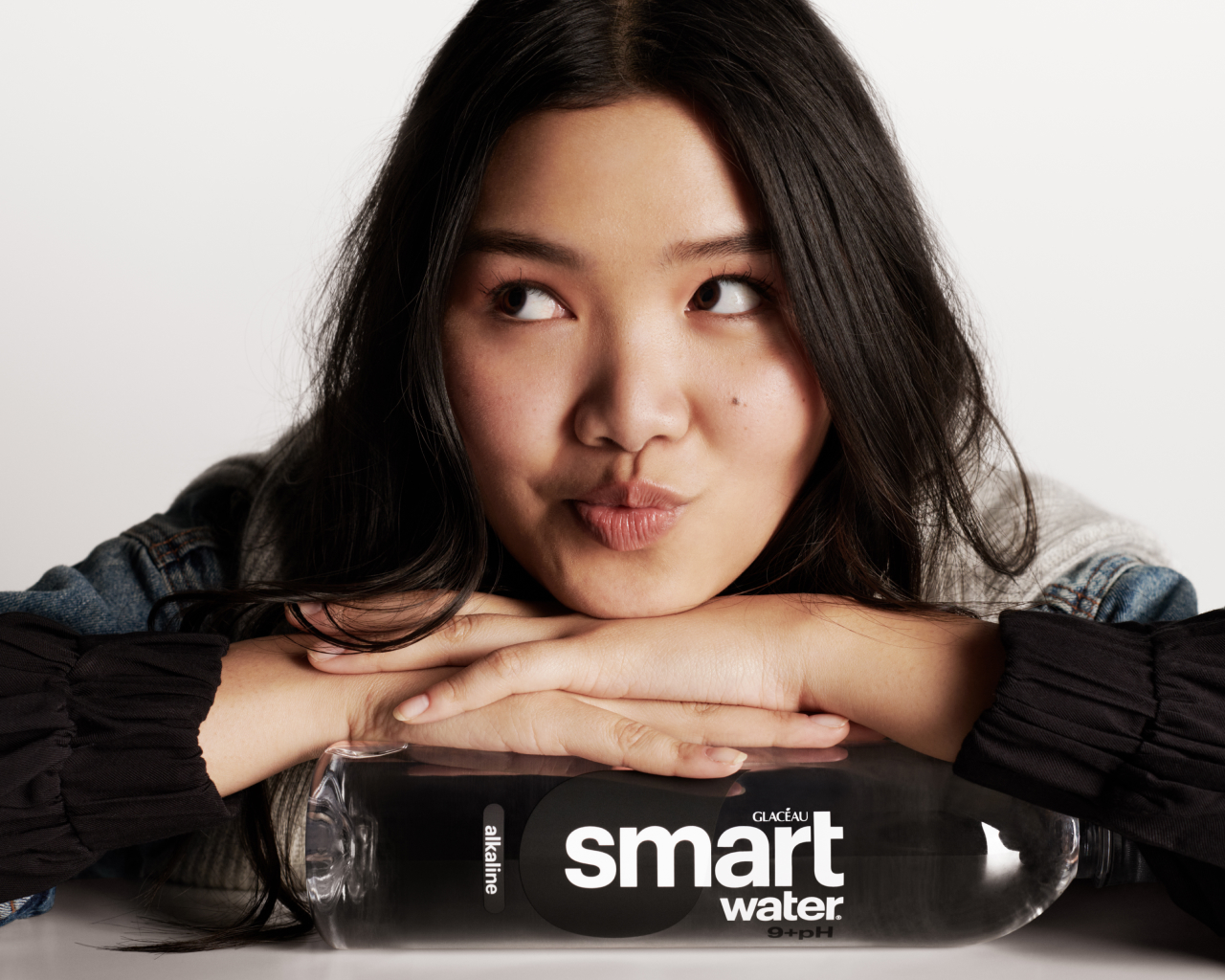 Woman posing with her face resting on her arms on top of a Glacéau Smartwater bottle