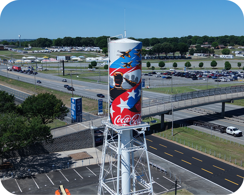 Wide view of Amber Thompson's patriotic Coca‑Cola mural painted on a tall water tower at the racetrack.