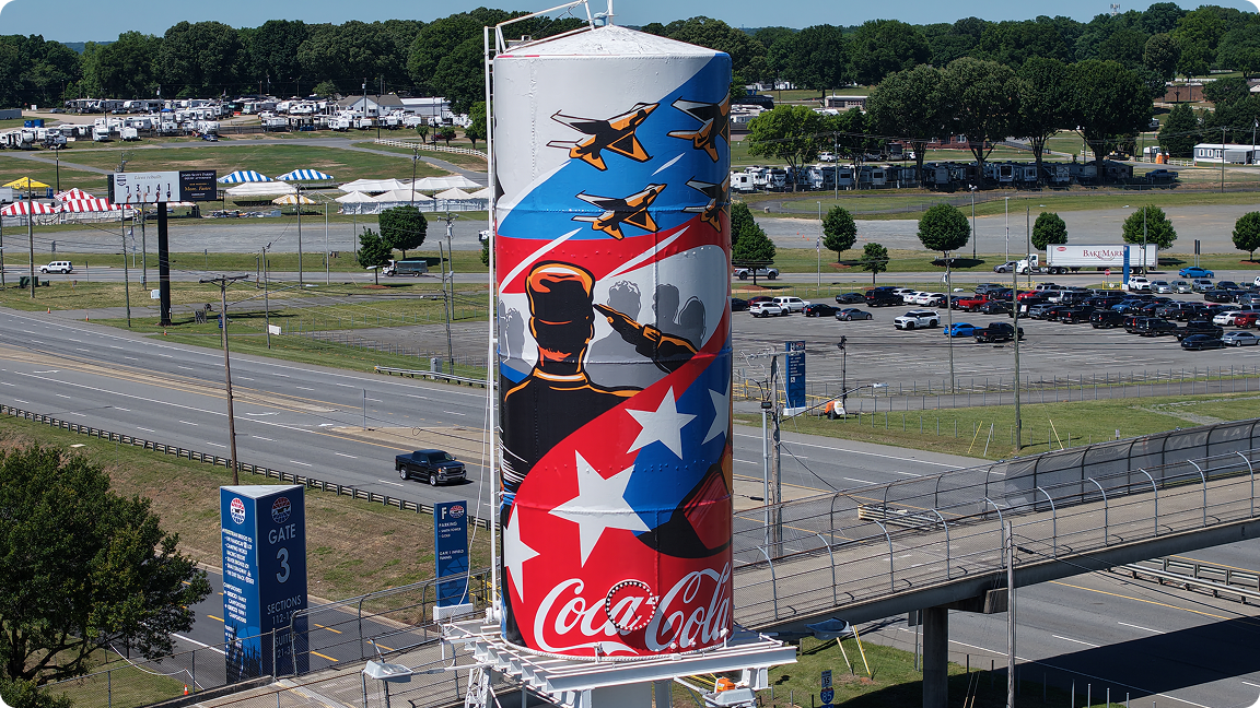 Wide landscape view of the Amber Thompson patriotic mural on the Coca-Cola water tower at Charlotte Motor Speedway.