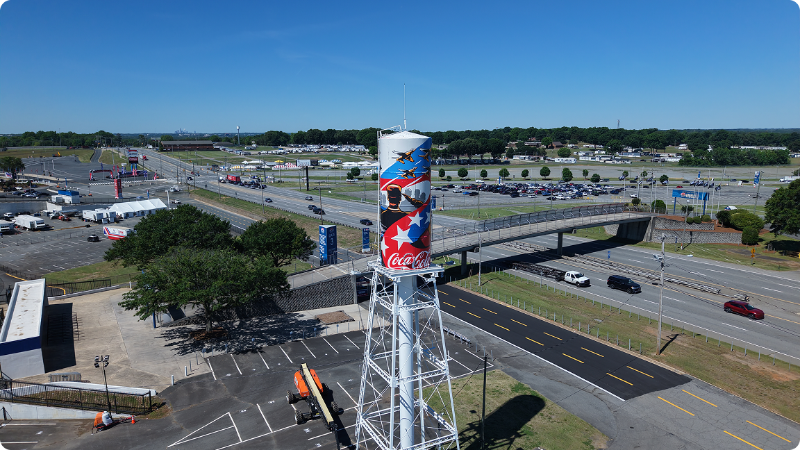 A distant, aerial shot of the patriotic Coca-Cola water tower mural, showing its location within the speedway grounds.