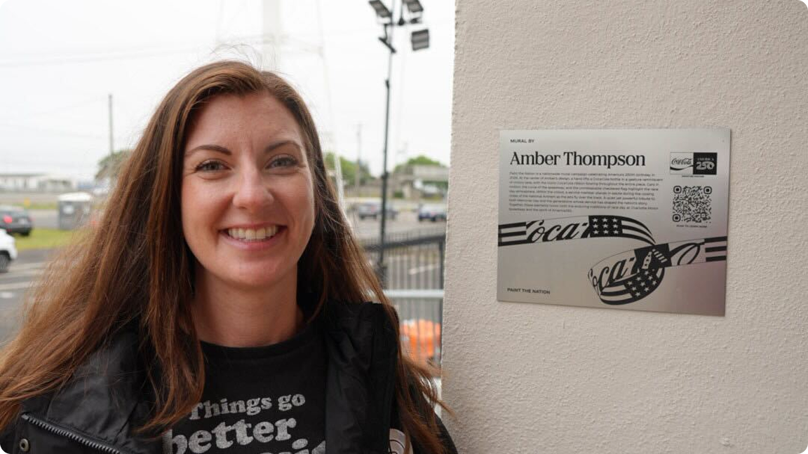 Artist Amber Thompson next to the descriptive plaque for her patriotic "Paint the Nation" Coca-Cola mural.