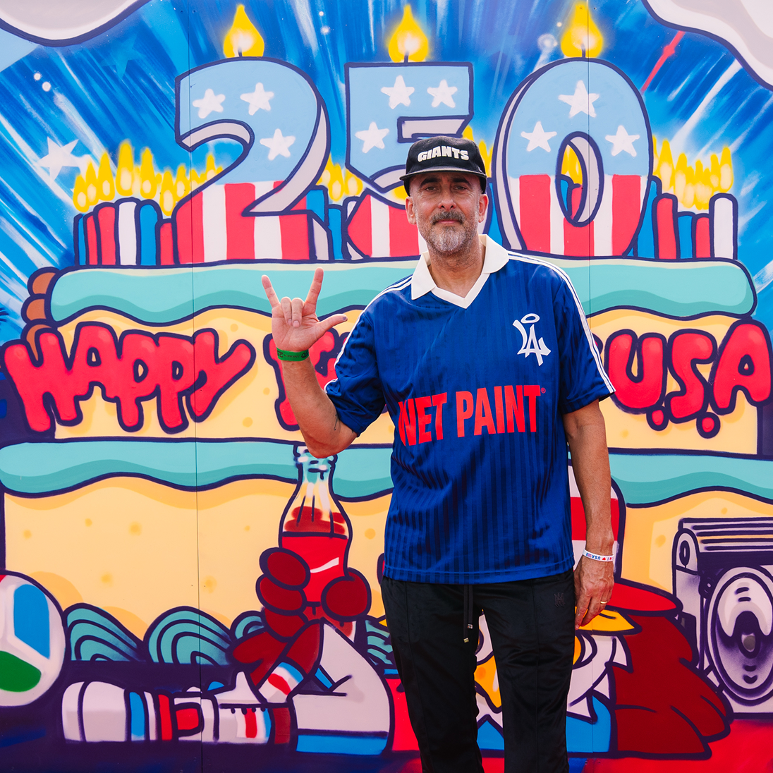 Artist Dave Ross posing in front of his colorful graffiti mural for the Coca‑Cola Paint the Nation campaign.