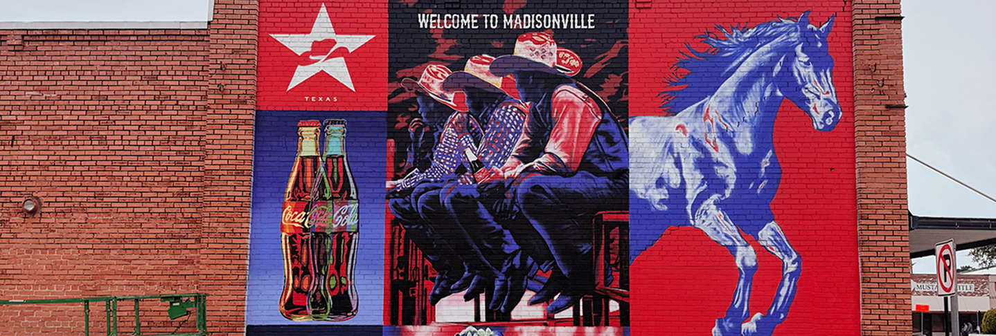A panoramic banner of the Coca-Cola mural in Madisonville, showing western themes and the "Welcome to Madisonville" text.