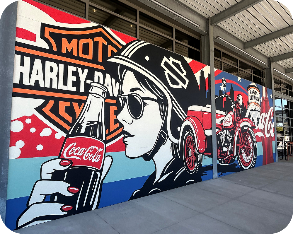 Wide view of Greg Gossel's mural showing a woman drinking Coca‑Cola next to a red Harley-Davidson motorcycle.