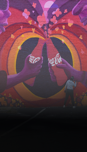 mural of two stylized figures clinking Coca-Cola bottles in pink and orange heart patterns