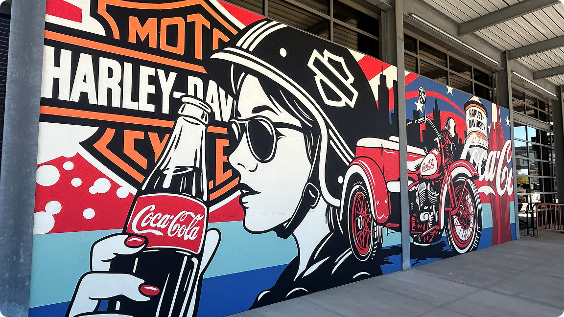 A woman in a pop-art style mural holds a classic Coca-Cola bottle in front of a Harley-Davidson logo shield.
