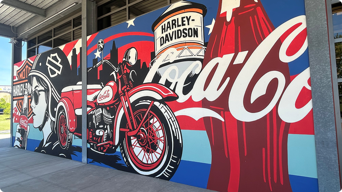 A close-up of a mural showing a large Coca-Cola bottle next to a water tower with the Harley-Davidson logo.