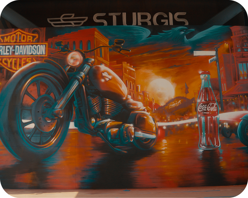 Close-up of the America 250 mural in Sturgis showing a Harley-Davidson motorcycle and Coca-Cola bottle.