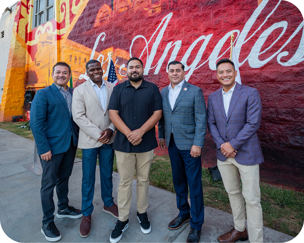 Five men posing in front of the colorful Los Angeles America 250 Coca-Cola mural at a dedication event.