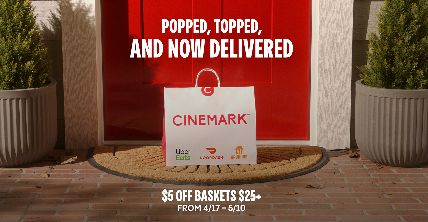 Cinemark popcorn and snacks delivery bag on doorstep promoting $5 off baskets $25+ with Uber Eats, DoorDash, and Grubhub