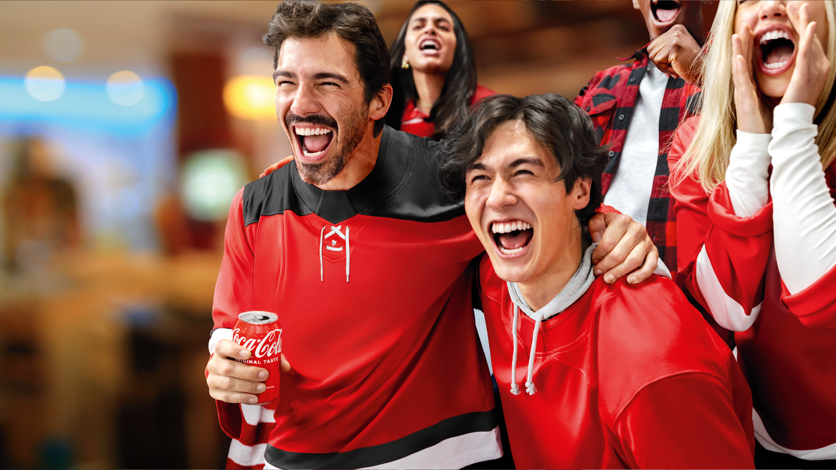 Excited hockey fans in red jerseys cheering together while holding a Coca-Cola can.