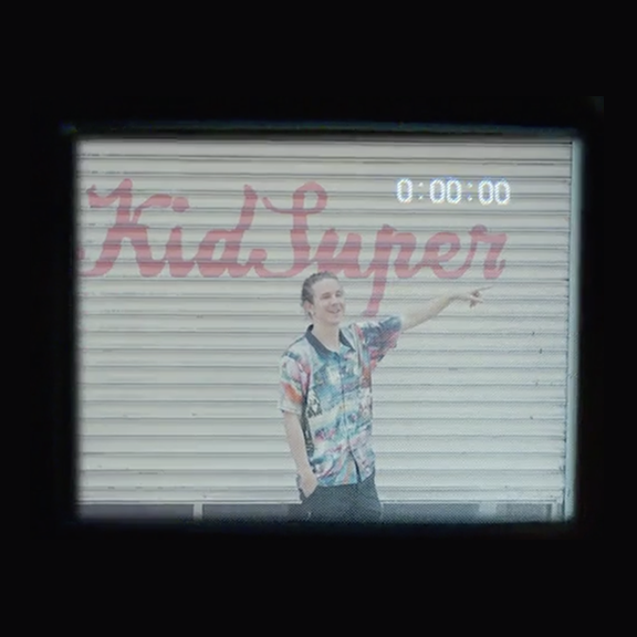 Retro VHS of a person standing in front of a garage door with Kid Super painted on it in script.