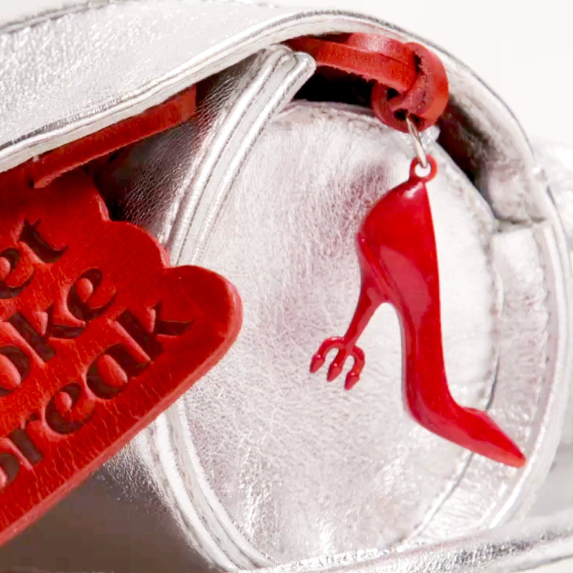 Close-up of red high heel charm and Diet Coke Break tag hanging from metallic silver Diet Coke Canny Pack bag