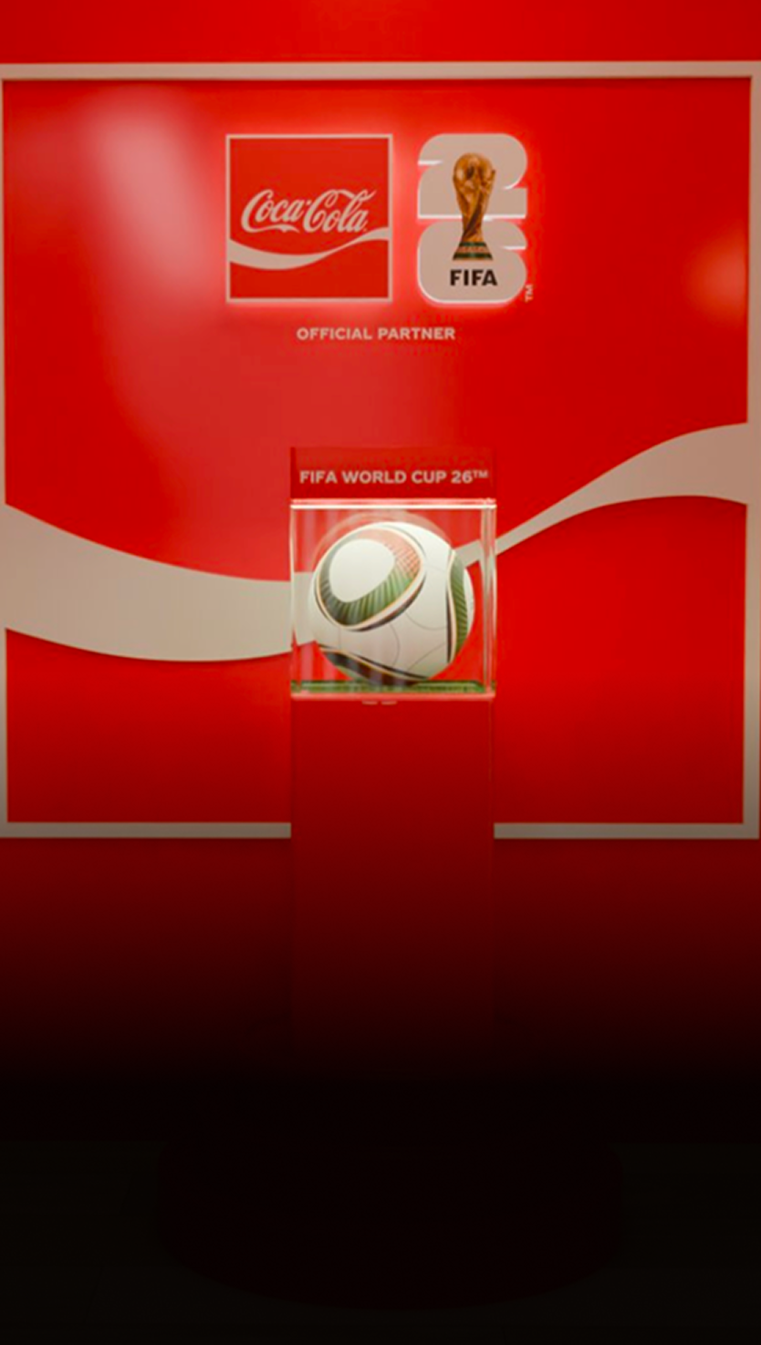 Official FIFA World Cup 26 match ball glowing in glass case on red Coca-Cola display pedestal inside the Fan Zone experience.
