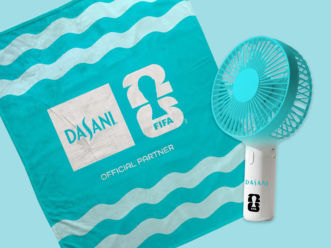 Turquoise DASANI and FIFA branded towel laid out beside matching handheld electric fan on light blue background.