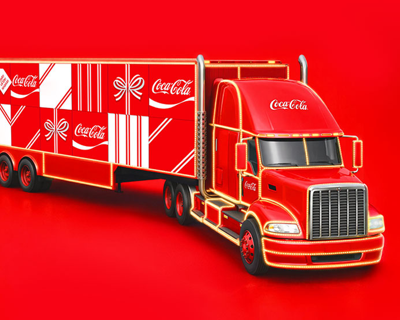 A red semi-truck outlined in glowing string lights sits on a solid red background. The Coca-Cola logo appears on the cab and the trailer, and the trailer is covered in red-and-white gift box patterns with ribbons and bows.