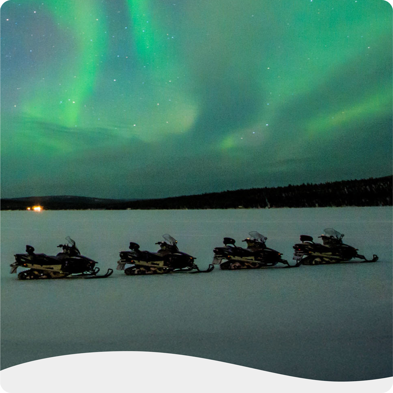 Four snowmobiles parked on a snowy expanse beneath a northern lights display