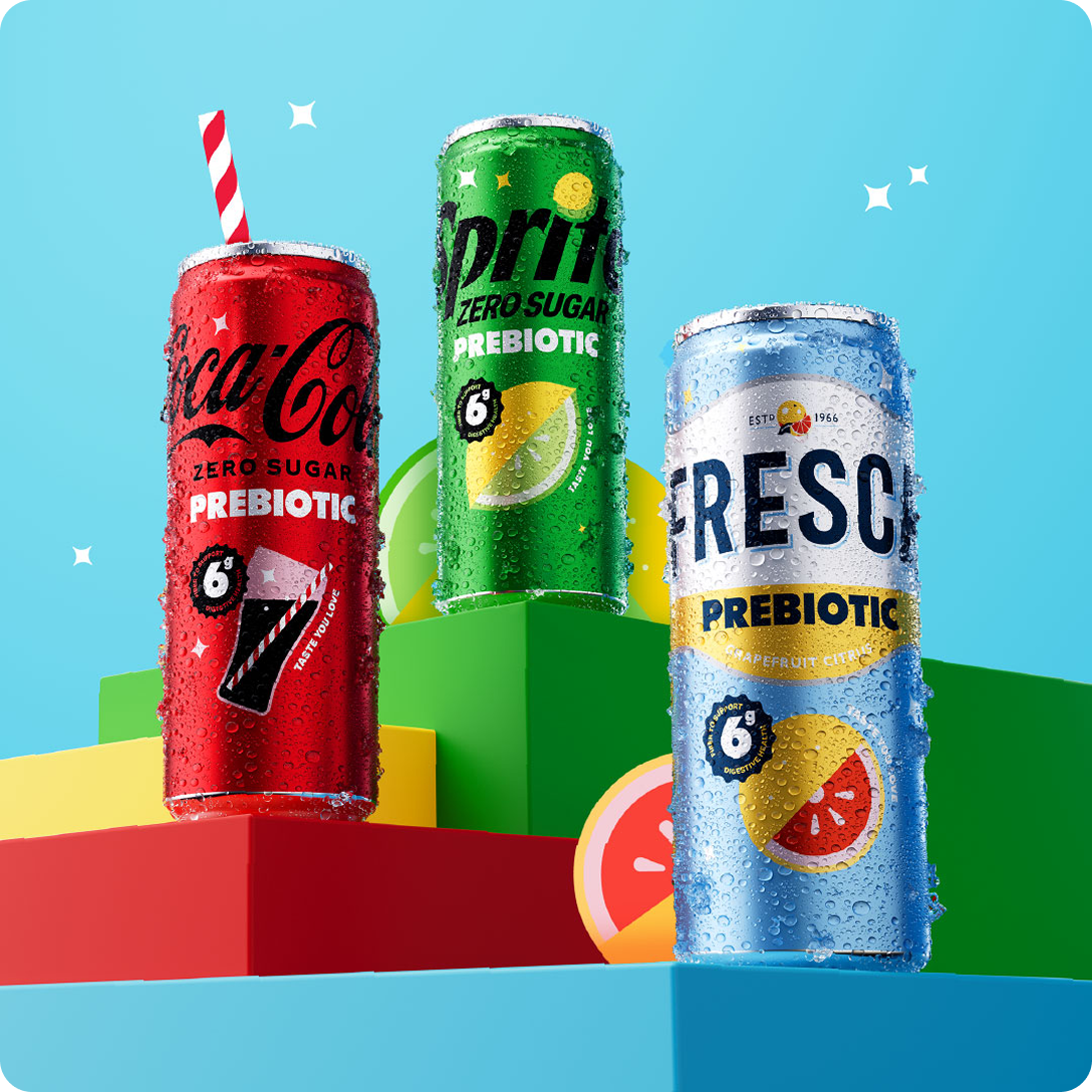 Three condensation-covered prebiotic soda cans displayed on colorful geometric blocks against a light blue background: Coca-Cola Zero Sugar Prebiotic (with a red-and-white straw), Sprite Zero Sugar Prebiotic, and Fresca Prebiotic Grapefruit Citrus, each marked with a "6g fiber to support digestive health" badge.