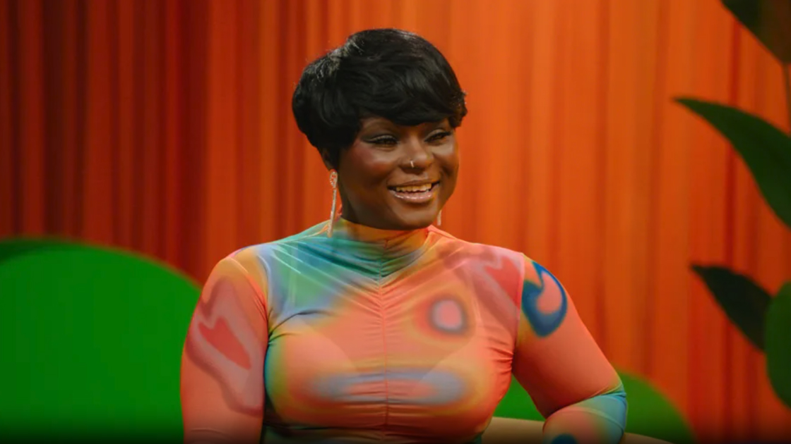 woman in bright colored shirt smiling in front of orange curtains