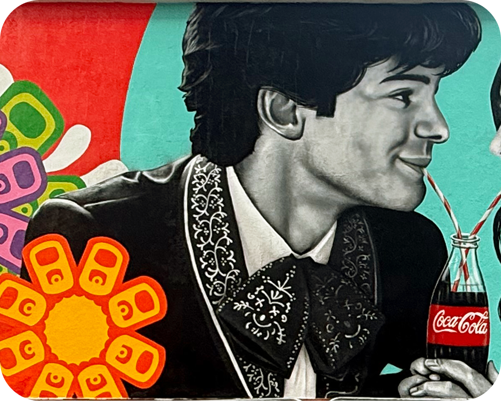 Acercamiento de un hombre con traje de charro compartiendo una Coca‑Cola en el mural Paint the Nation de Los Otros.