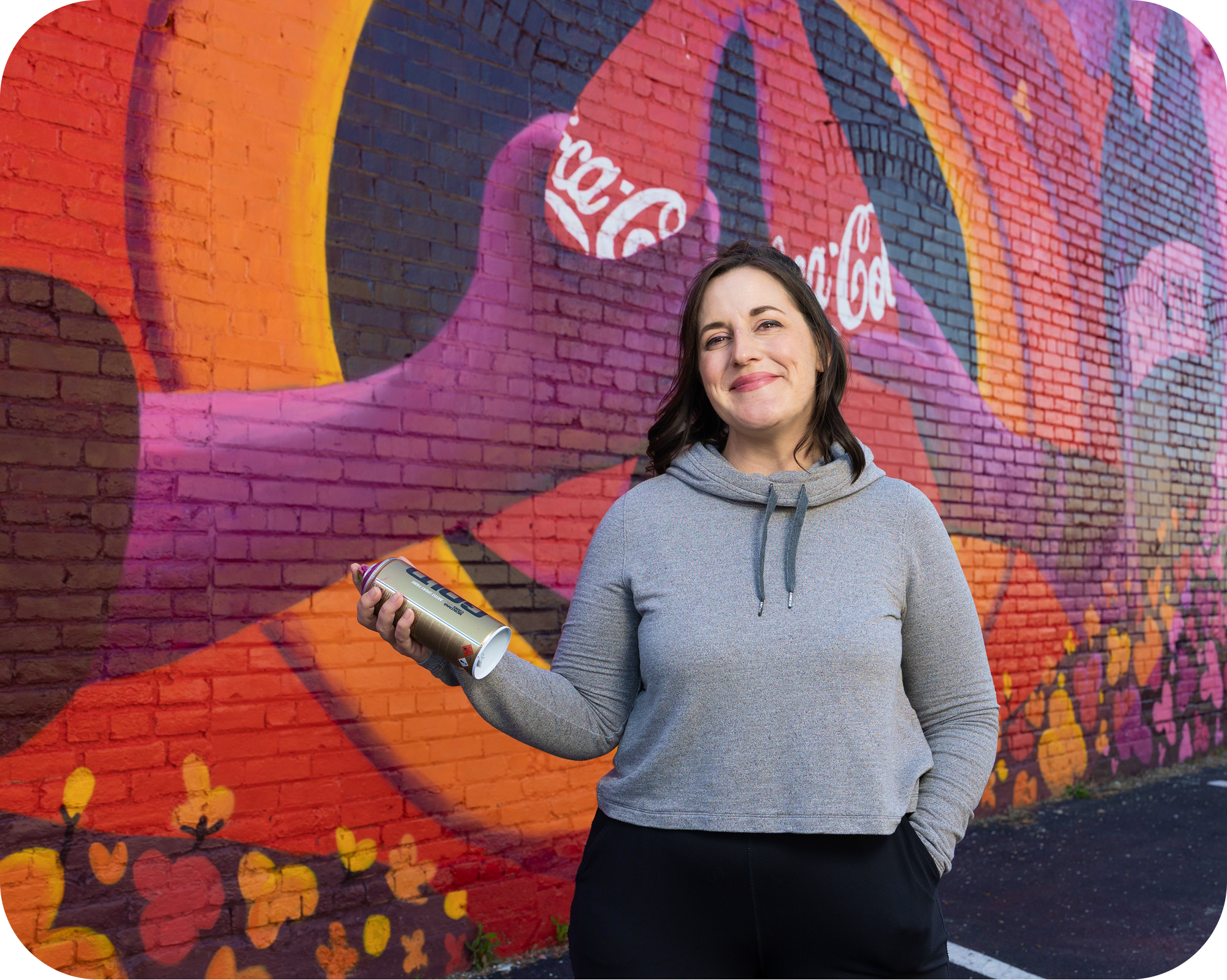 Meg Wagler pintando un colorido mural de Coca‑Cola mientras es filmada por un equipo de grabación.