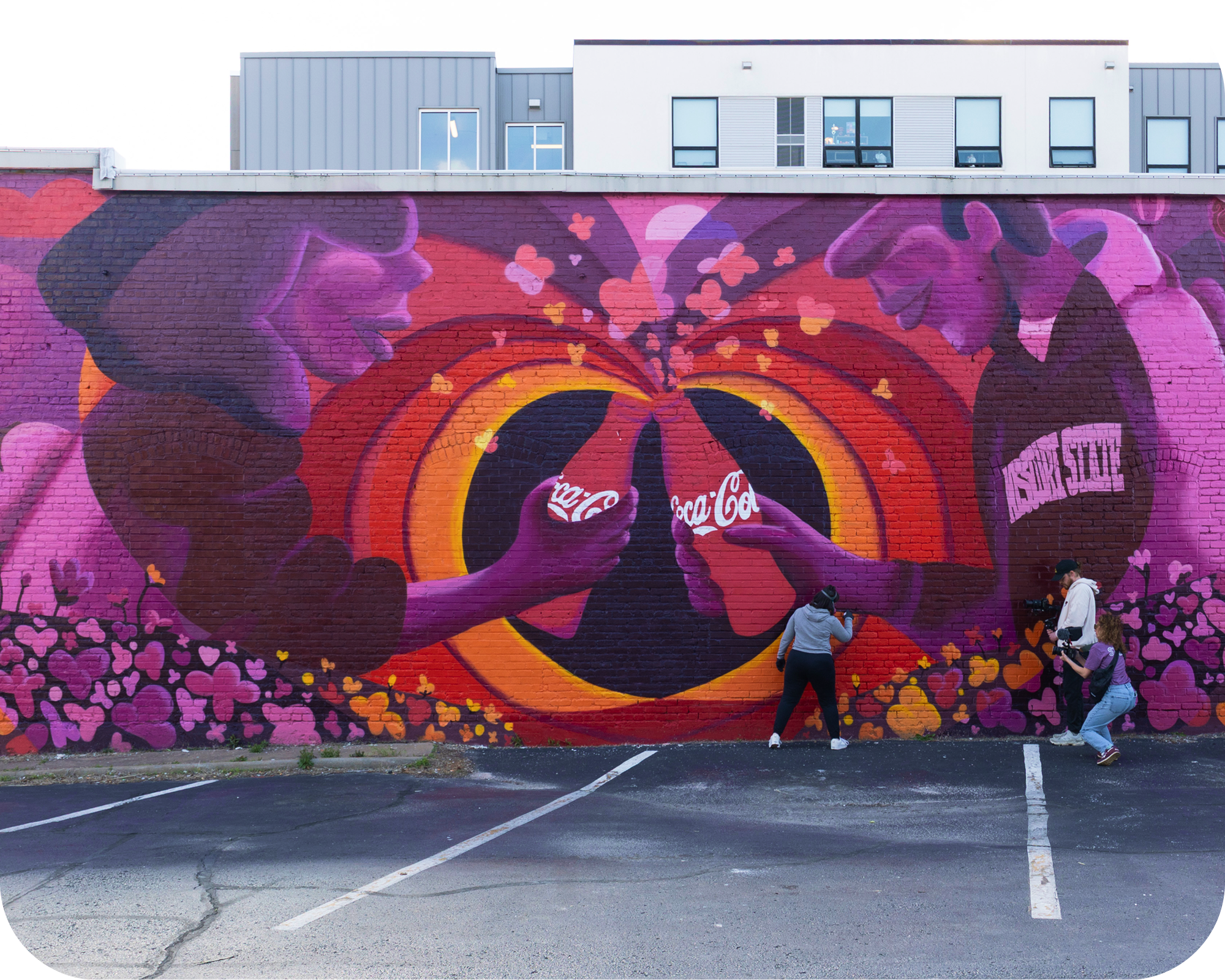 La artista Meg Wagler posando con confianza frente a su mural terminado de Coca‑Cola.