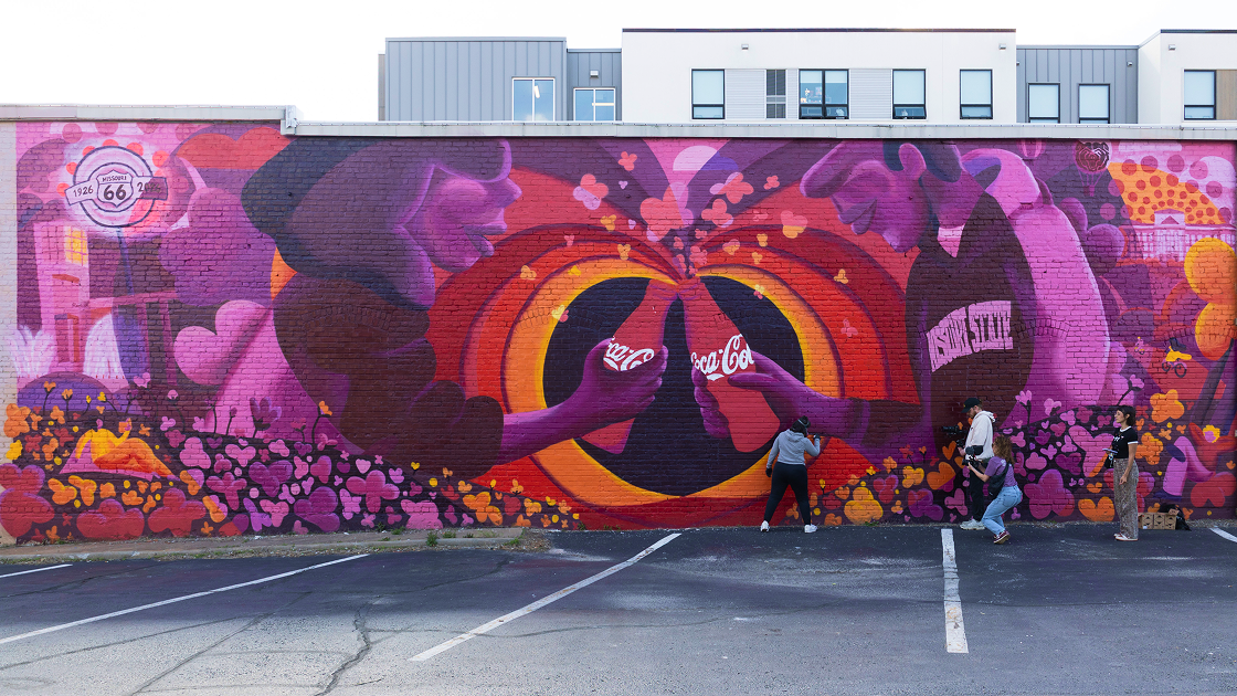 Equipo pintando el mural Paint the Nation de Coca-Cola, rodeado de corazones naranjas y rosas
