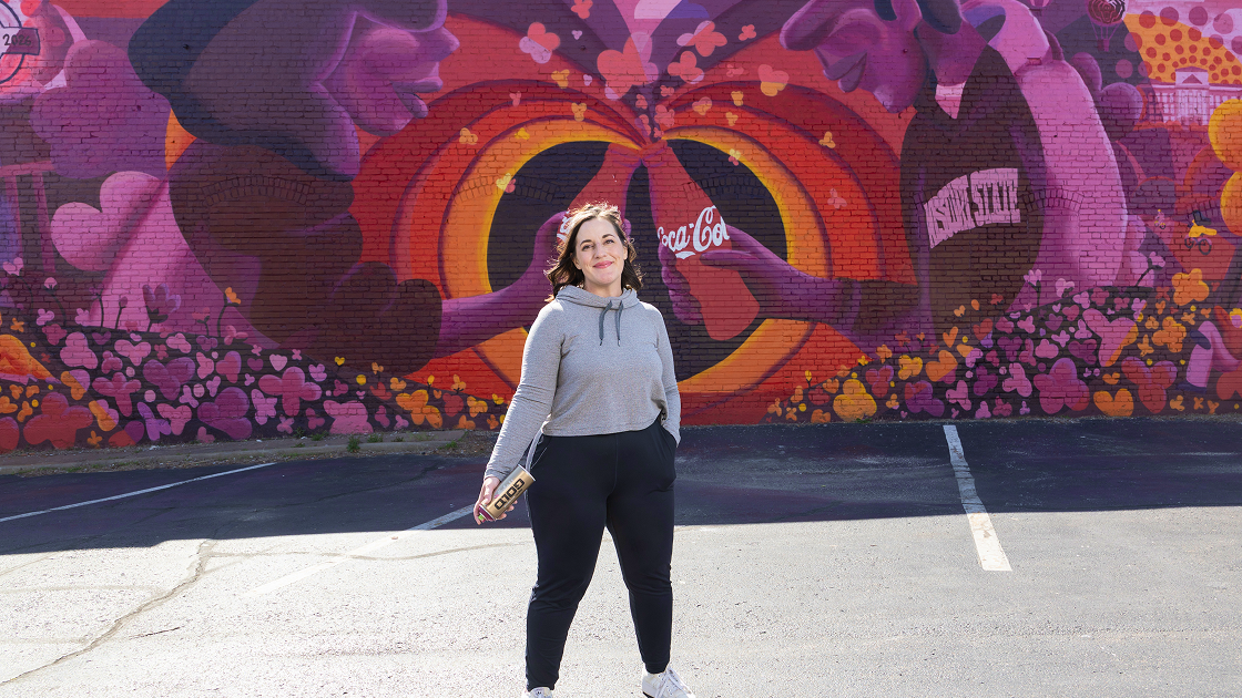 Artista posando frente al mural Paint the Nation de Coca-Cola terminado, con corazones vibrantes llenando la pared