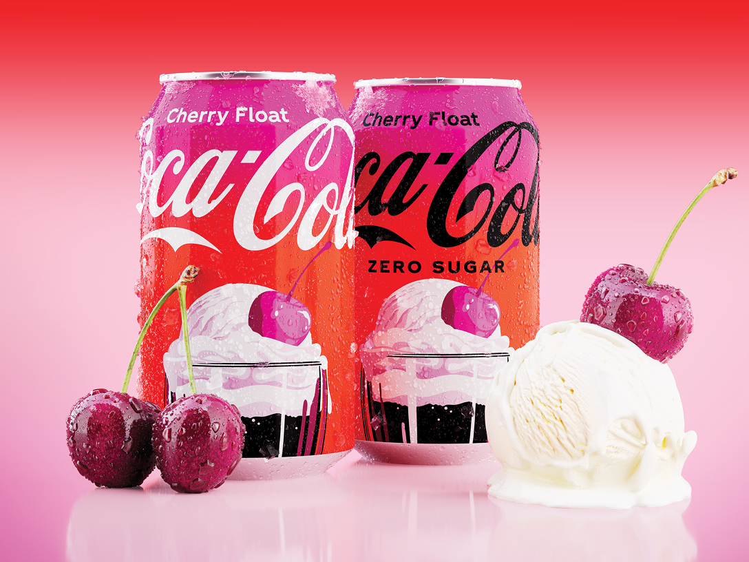 Dos latas de Coca-Cola sabor Cherry Float (una versión regular y una Zero Sugar) están colocadas juntas sobre fondo rojo y rosado degradado, mostrando una ilustración de una copa con helado de vainilla y una cereza encima. Frente a las latas hay cerezas frescas y una porción de helado de vainilla, todo con gotas de agua que sugieren frescura.