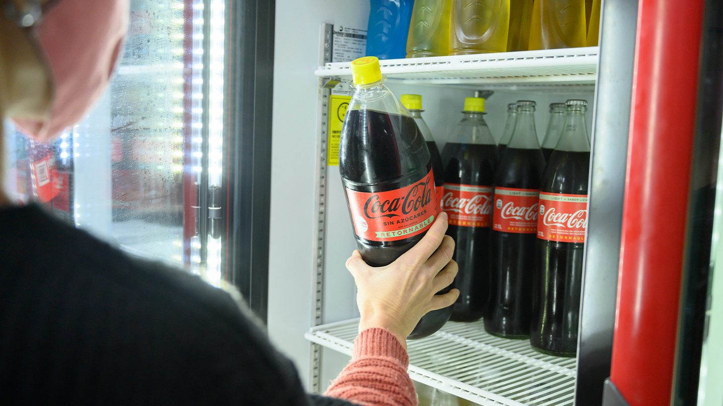 Mano tomando una botella de Coca-Cola de una heladera