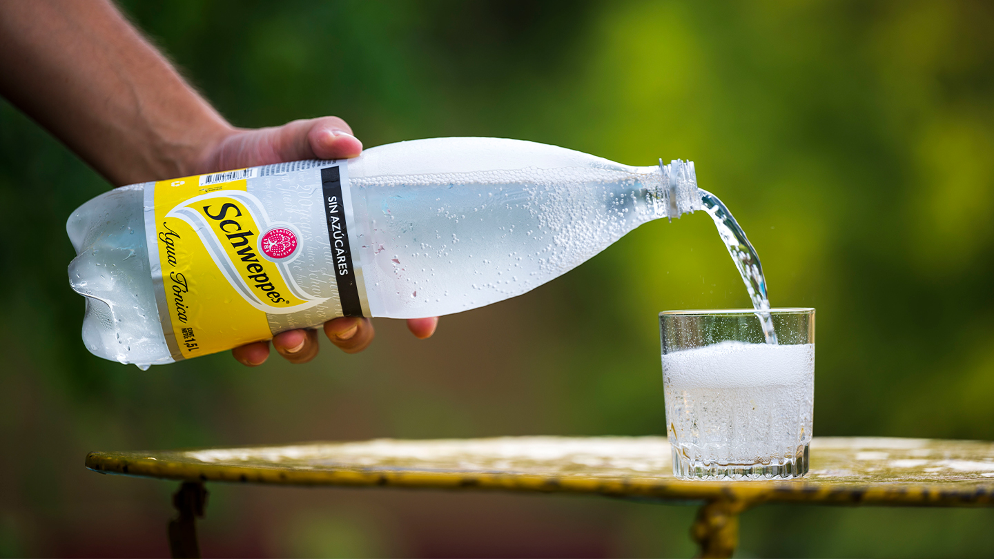 Mano vertiendo botella Schweppes en un vaso