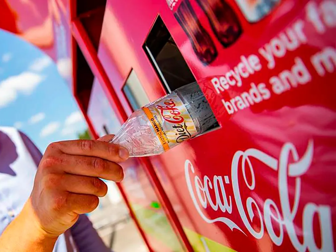 Detalhe de uma mão de uma pessoa colocando uma garrafa vazia de Coca-Cola Diet em uma lixeira reciclável da Coca-Cola