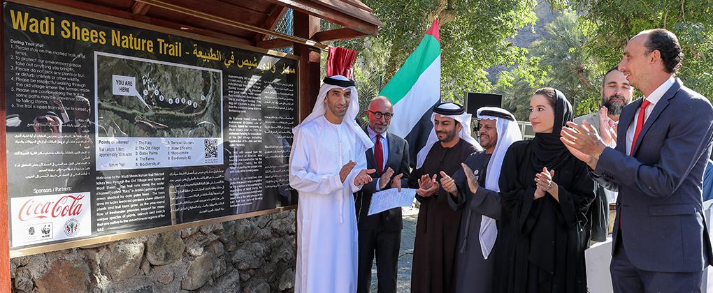 A group of people clapping hands next to a sign that shows information about the Wadi Shees Nature Trail 