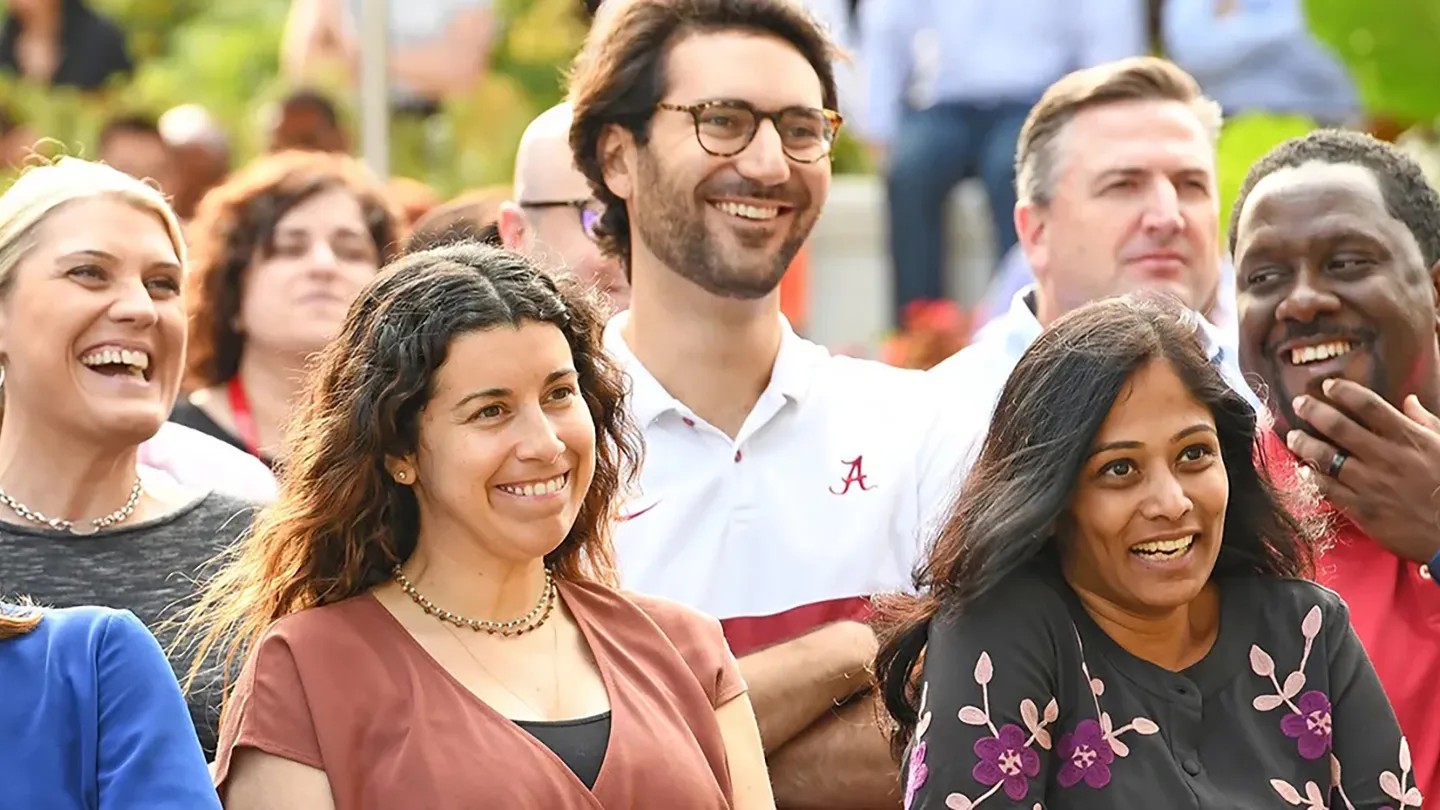 A large group of people laughing and smiling while watching something outdoors