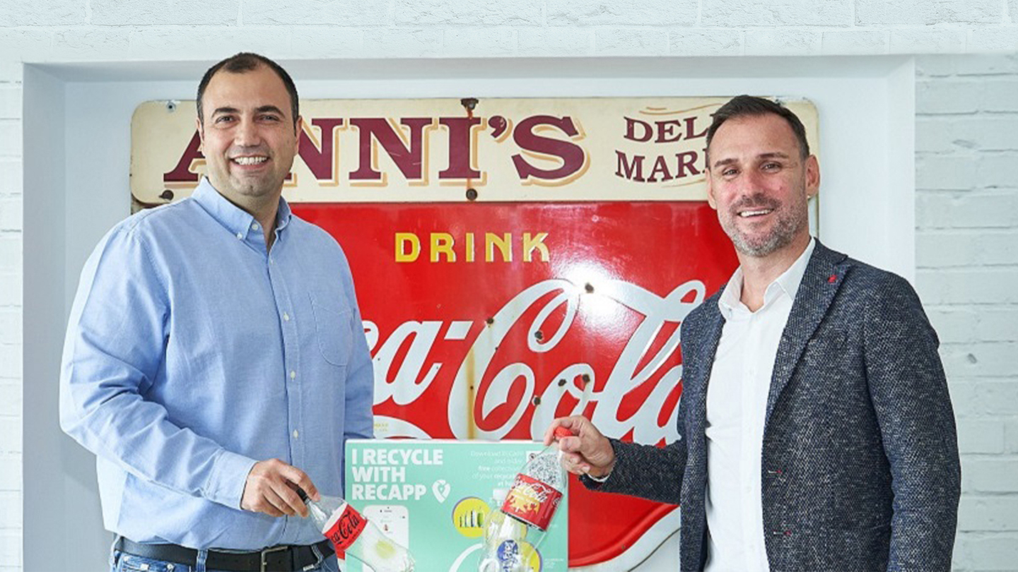 Two men with a plastic Coca-Cola bottle encourage people to recycle.