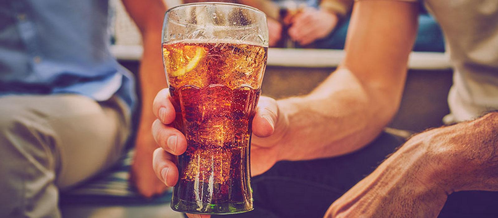 A person holding a large glass of Coca-Cola with ice