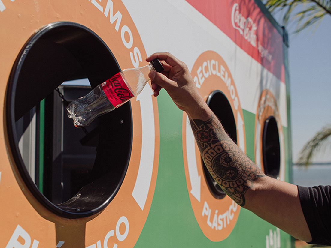 Detail of a hand putting an empty Coca-Cola plastic bottle in a recyclable trash bin