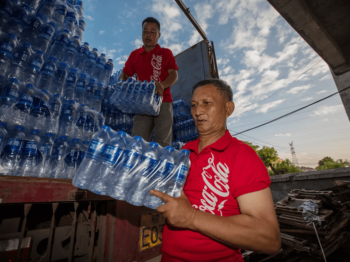 Двоє чоловіків розвантажують пакети бутильованої води з вантажівки
