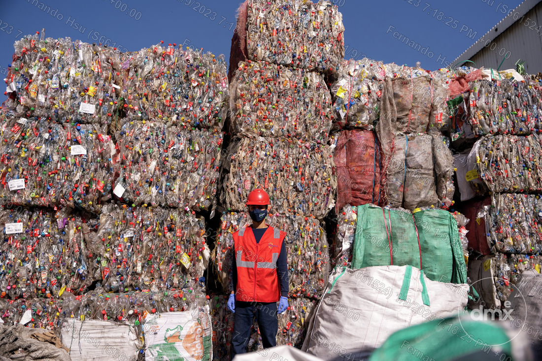 A man with a red safe vest in front of several stacked plastic piles